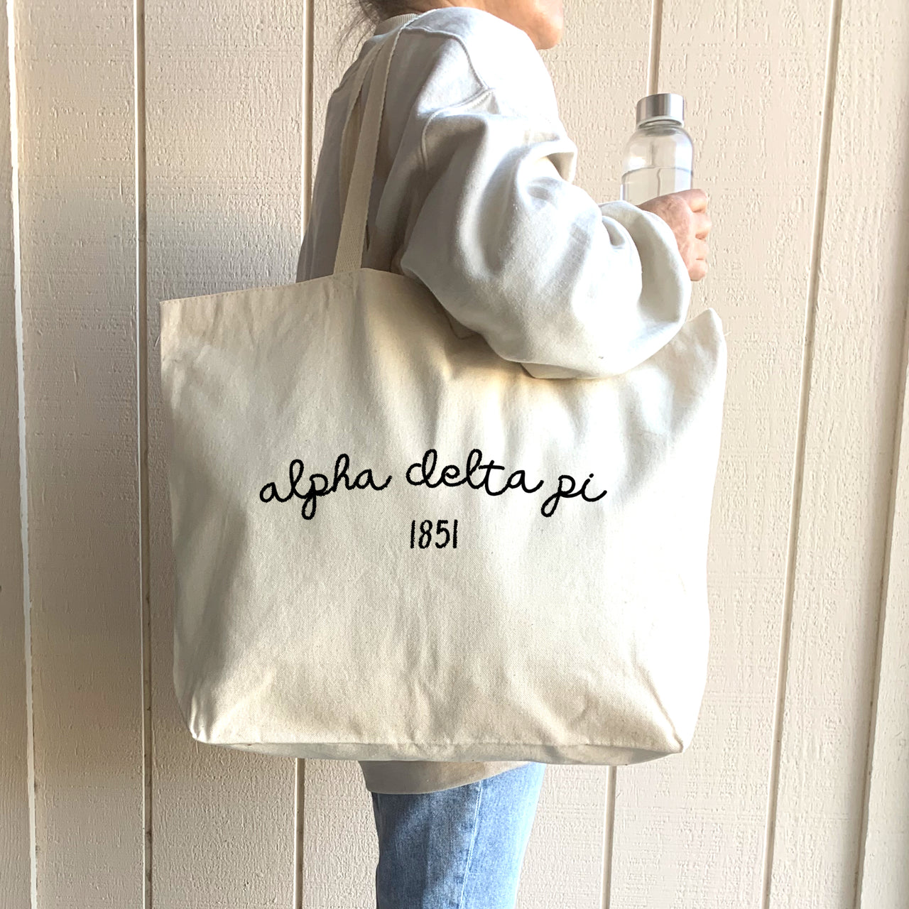 A cheerful student walks across campus with an Alpha Delta Pi canvas tote, perfect for carrying books, school supplies, and daily must-haves.