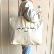 A stylish young woman models her Alpha Gamma Delta tote bag, proudly showcasing her sorority affiliation with a bold and elegant design.