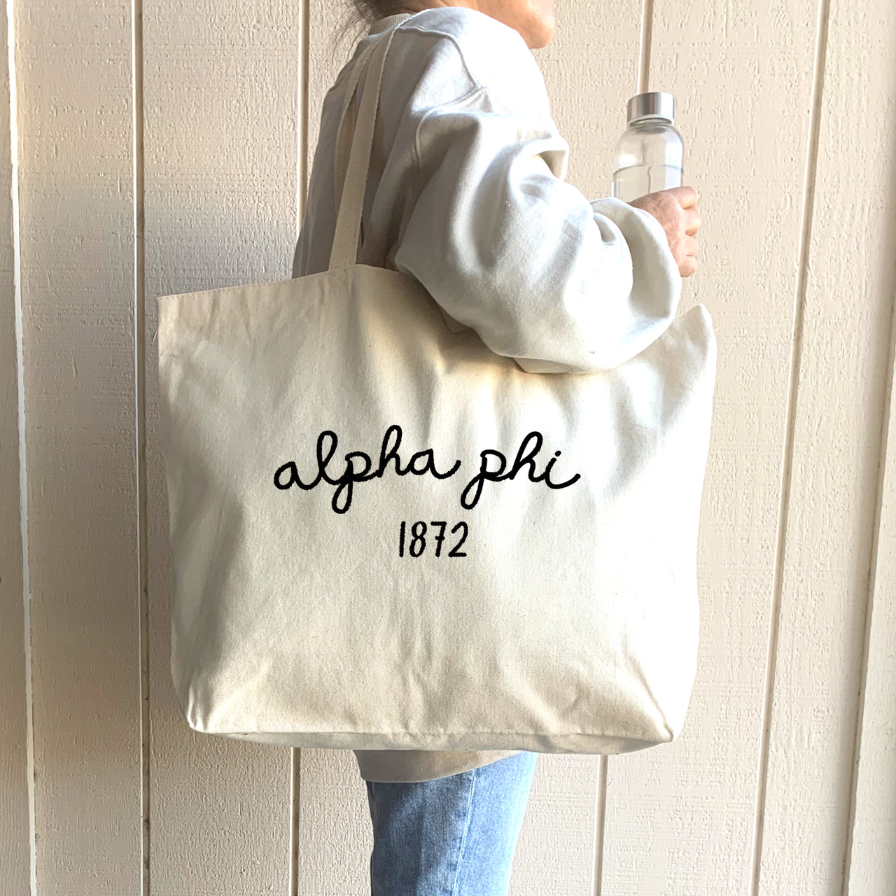 A college student carries her Alpha Phi tote bag across campus, blending style and practicality in an everyday sorority essential.