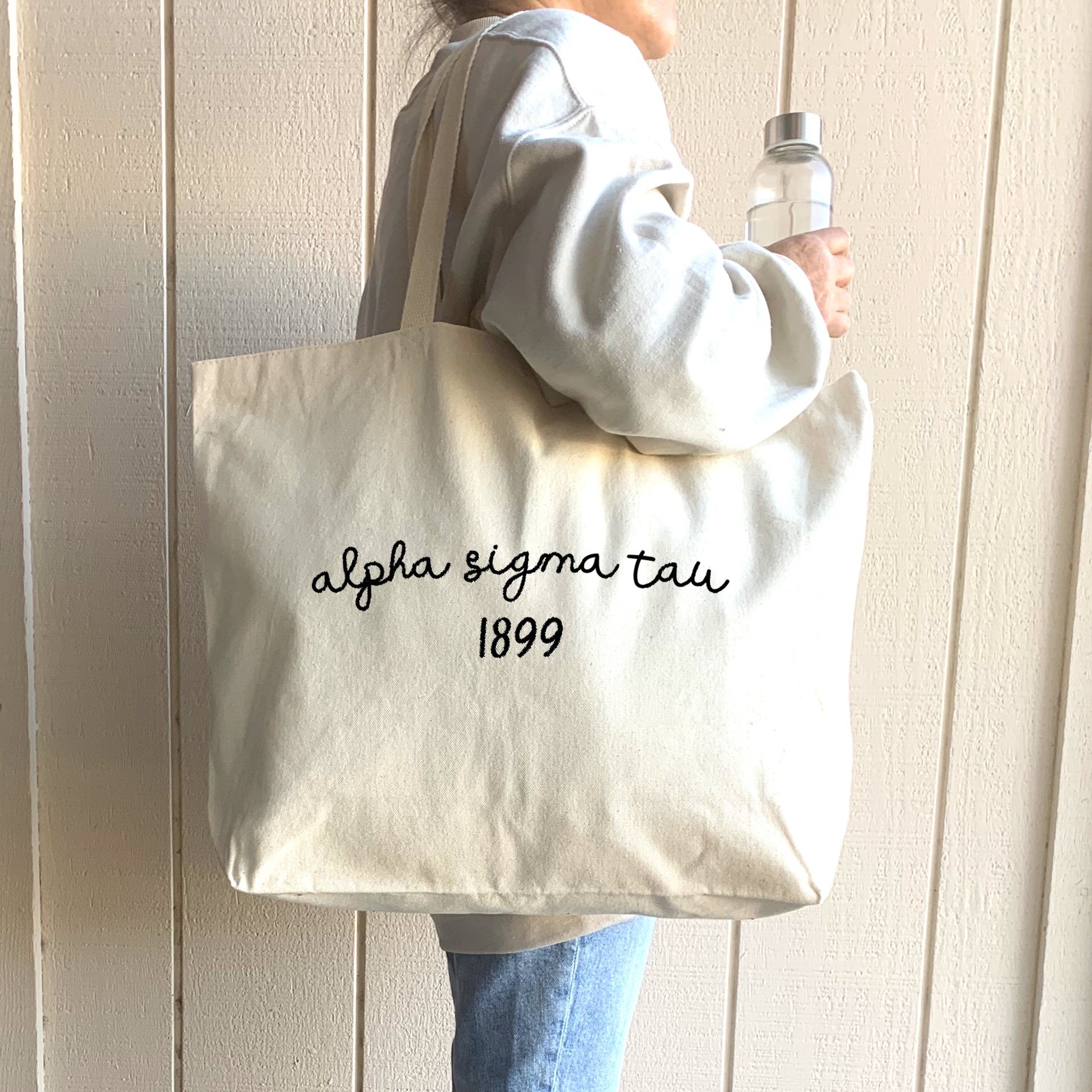 Alpha Sigma Tau – A young woman showcases her Alpha Sigma Tau tote bag, perfect for carrying notebooks and sorority essentials.