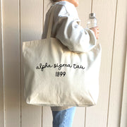 A student showcases her Alpha Sigma Tau tote bag, a must-have for carrying study materials, sorority gifts, or daily essentials.