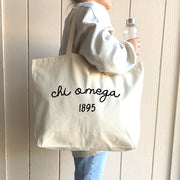 Chi Omega – A college student proudly wears a Chi Omega tote bag over her shoulder, embodying the spirit of sisterhood and style.