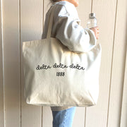 Delta Delta Delta – A trendy student walks through campus with a Delta Delta Delta sorority tote, a versatile and stylish Greek life accessory.