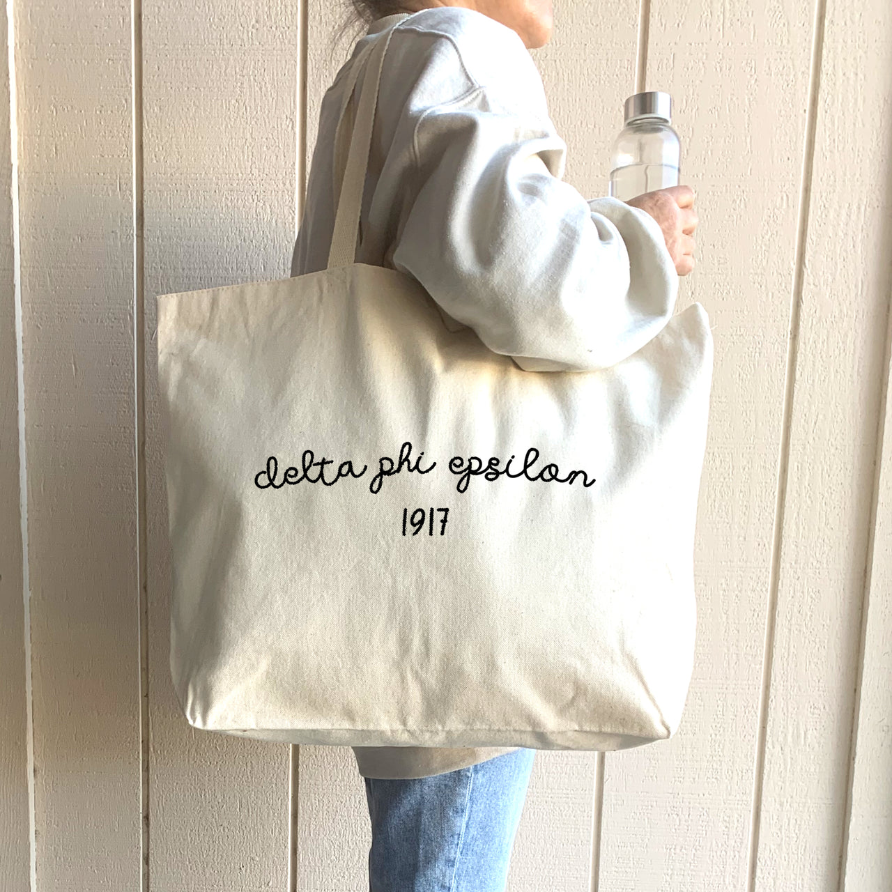 A student poses with her Delta Phi Epsilon tote, highlighting its spacious design and personalized Greek lettering.