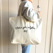 Theta Phi Alpha – A student models her Theta Phi Alpha sorority tote bag, a must-have for Bid Day, recruitment, or daily essentials.