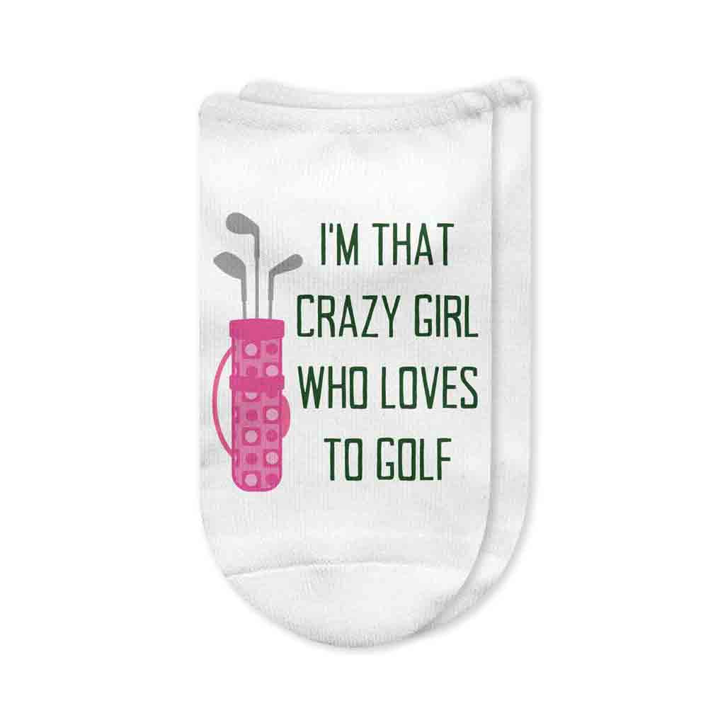 A pair of white no-show golf socks with the phrase "I'm That Crazy Girl Who Loves to Golf" printed on top in bold lettering, perfect for passionate women golfers who bring energy to the course. A fun and unique golf gift.