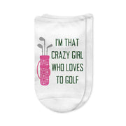 A pair of white no-show golf socks with the phrase "I'm That Crazy Girl Who Loves to Golf" printed on top in bold lettering, perfect for passionate women golfers who bring energy to the course. A fun and unique golf gift.