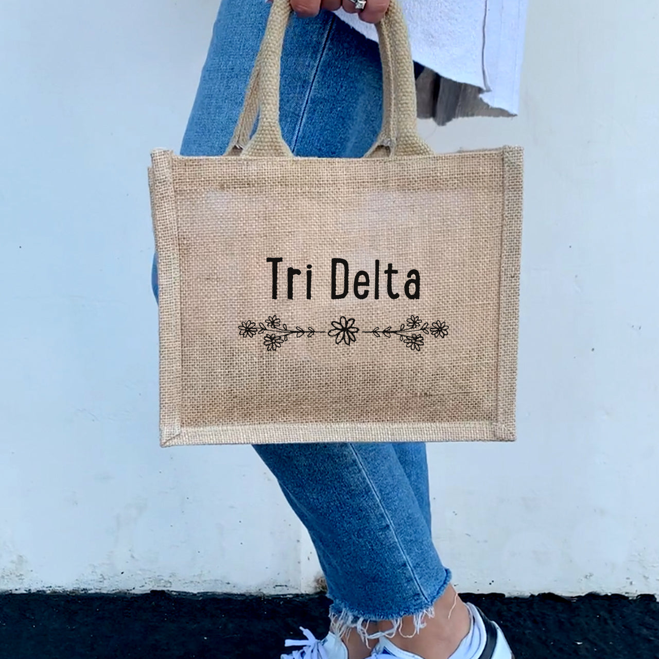 A model showing off the Delta Delta Delta floral burlap tote, an ideal accessory for any sorority sister on the go.