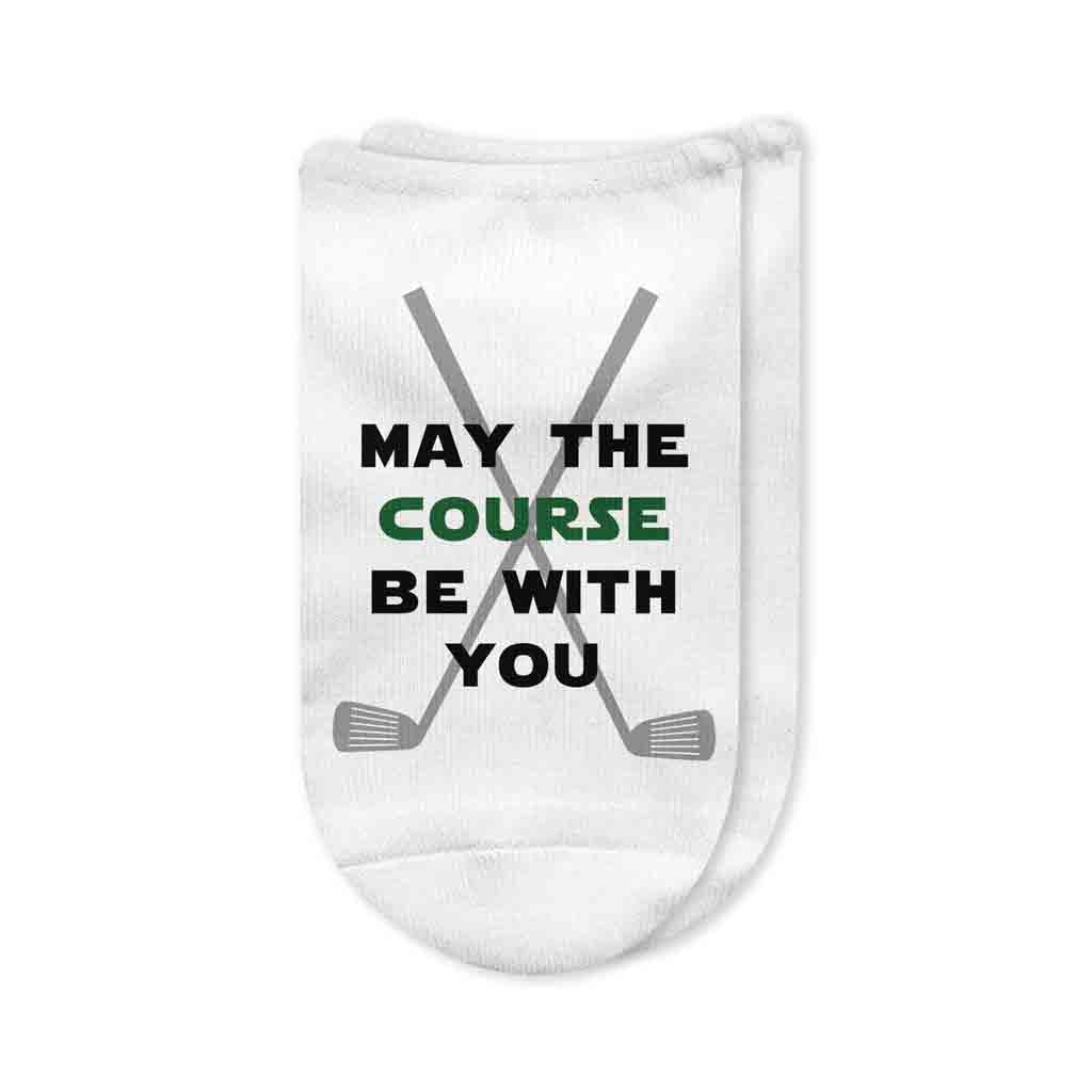 A pair of white no-show golf socks with the phrase "May The Course Be With You" printed on top in bold black lettering. The socks feature a soft cotton/poly blend with a cushioned sole, designed for comfort on the golf course. A fun and unique gift for golfers and Star Wars fans.