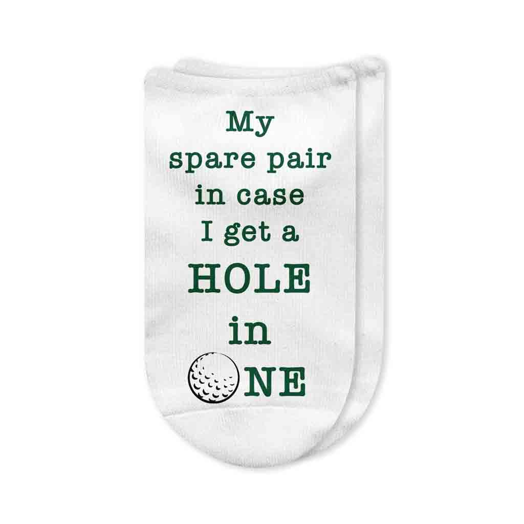 A pair of white no-show golf socks with the phrase "My Spare Pair in Case I Get a Hole in One" printed on top, designed for men golfers. A fun and practical golf gift or tournament prize.