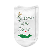 A pair of white no-show golf socks with the phrase "Queen of the Greens" printed on top in stylish lettering, perfect for women golfers who rule the course. A fun and comfortable golf gift.